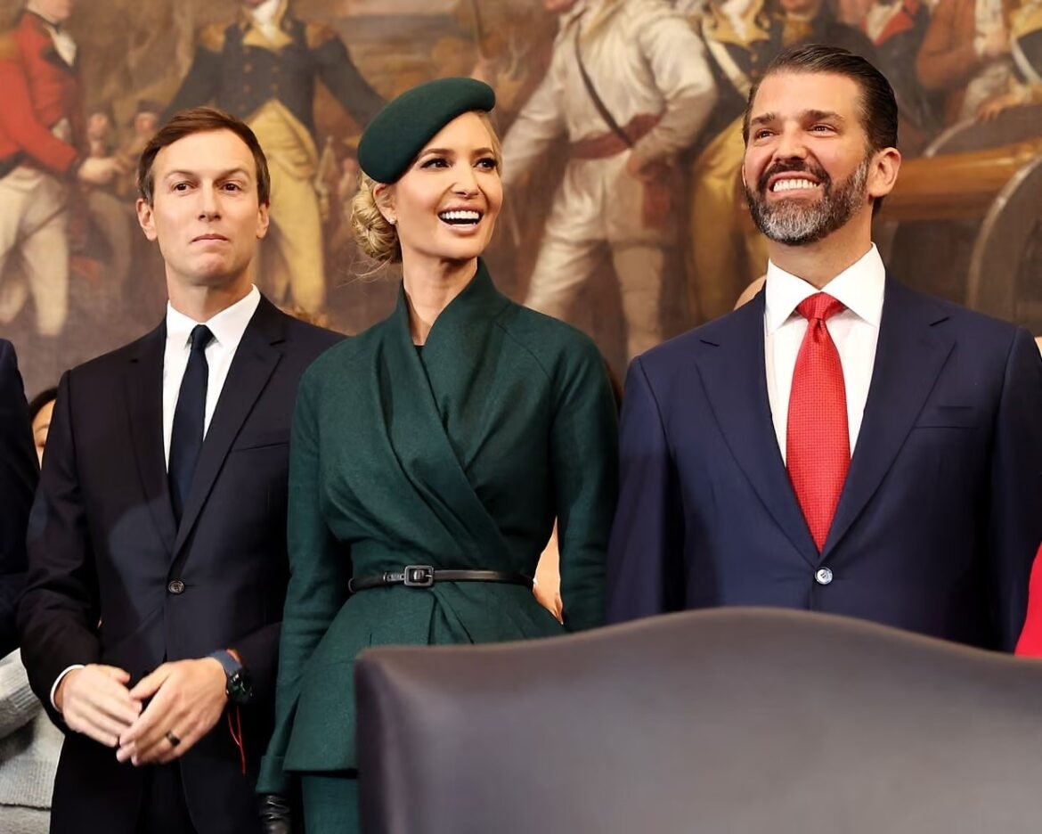 Three adults in formal attire at an event; a woman in a dark green belted outfit and beret stands between two men in suits, smiling.