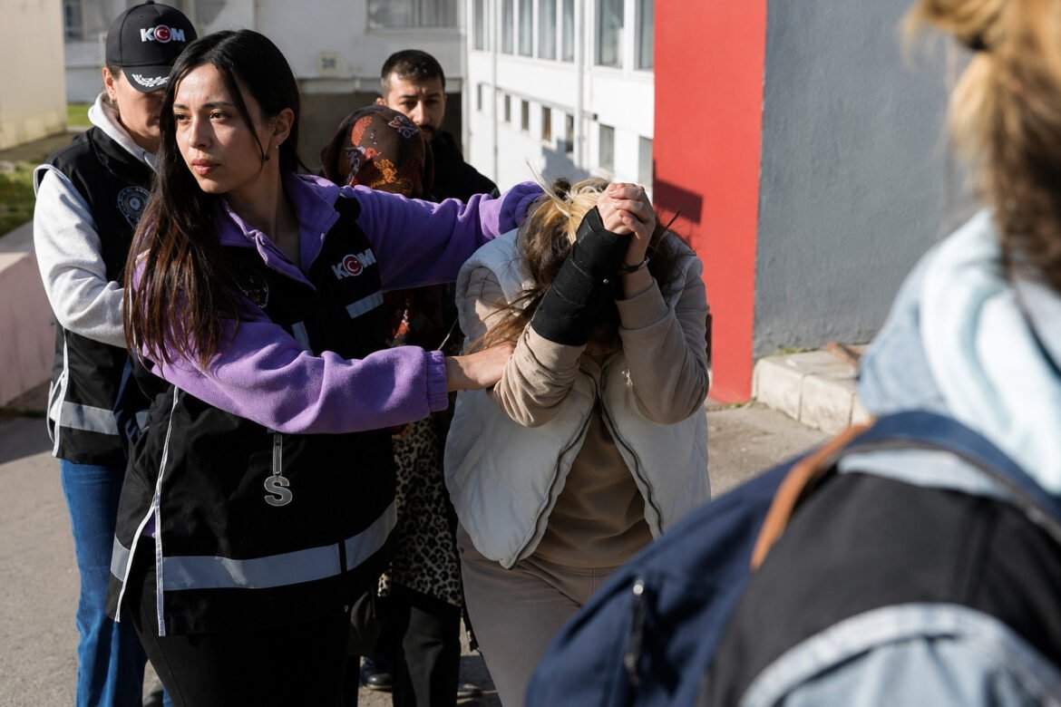 Group of people in vests restraining a distressed woman outdoors near a building (likely a training drill).