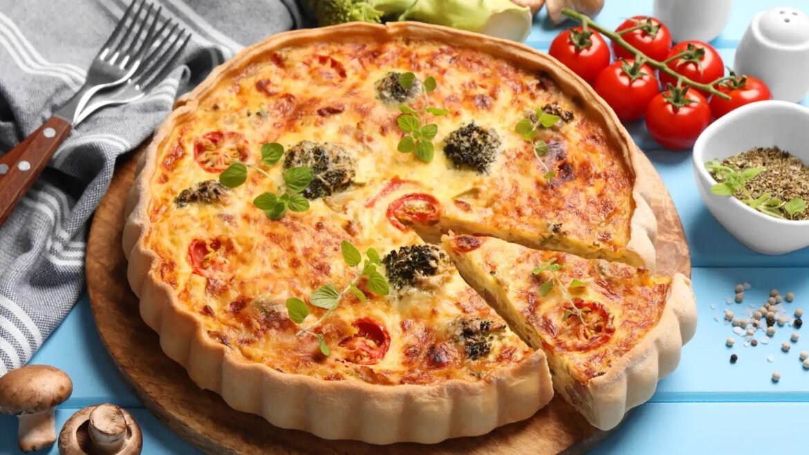 Savory quiche with tomatoes, broccoli, and cheese on a thick golden crust, garnished with fresh herbs on a wooden board.