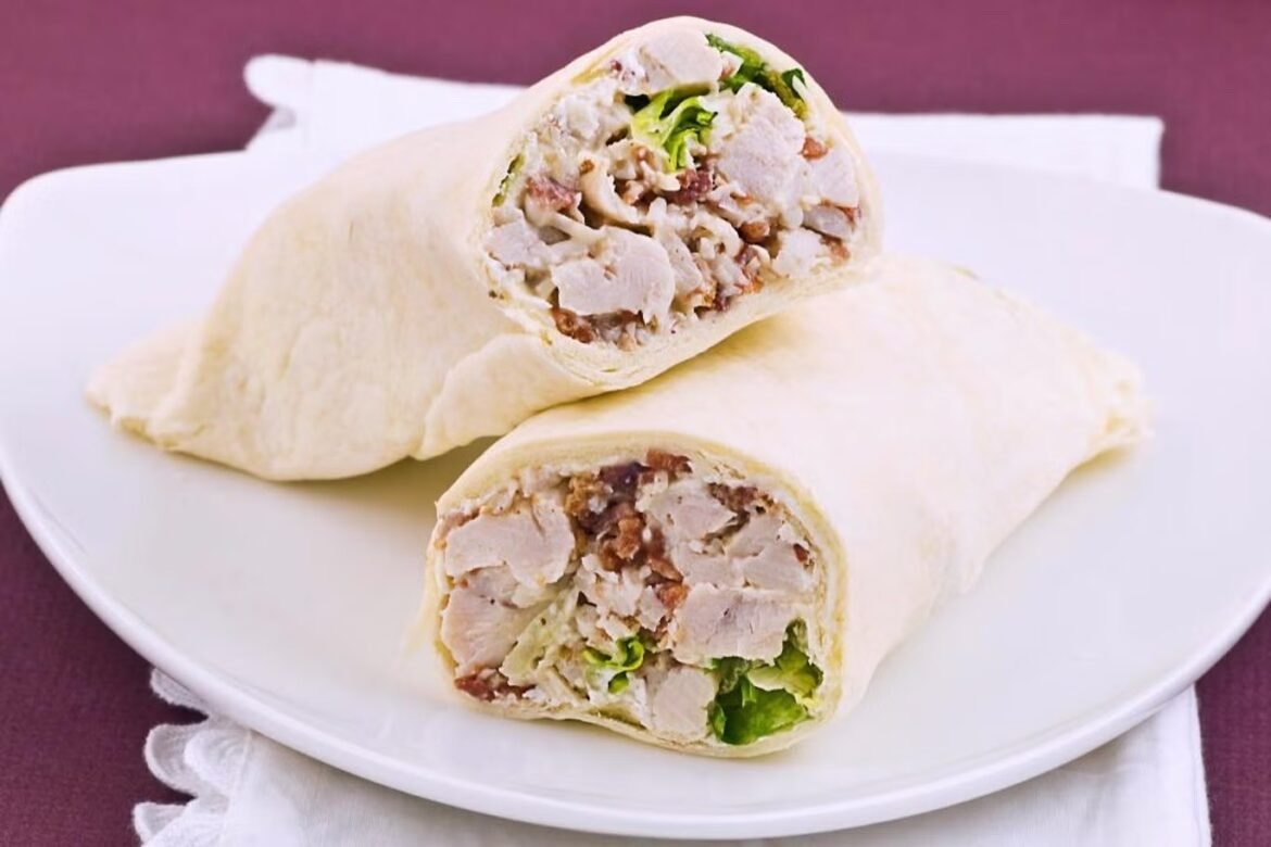 Two halved chicken wraps on a white plate, revealing diced chicken, lettuce, and veggies inside a soft tortilla.