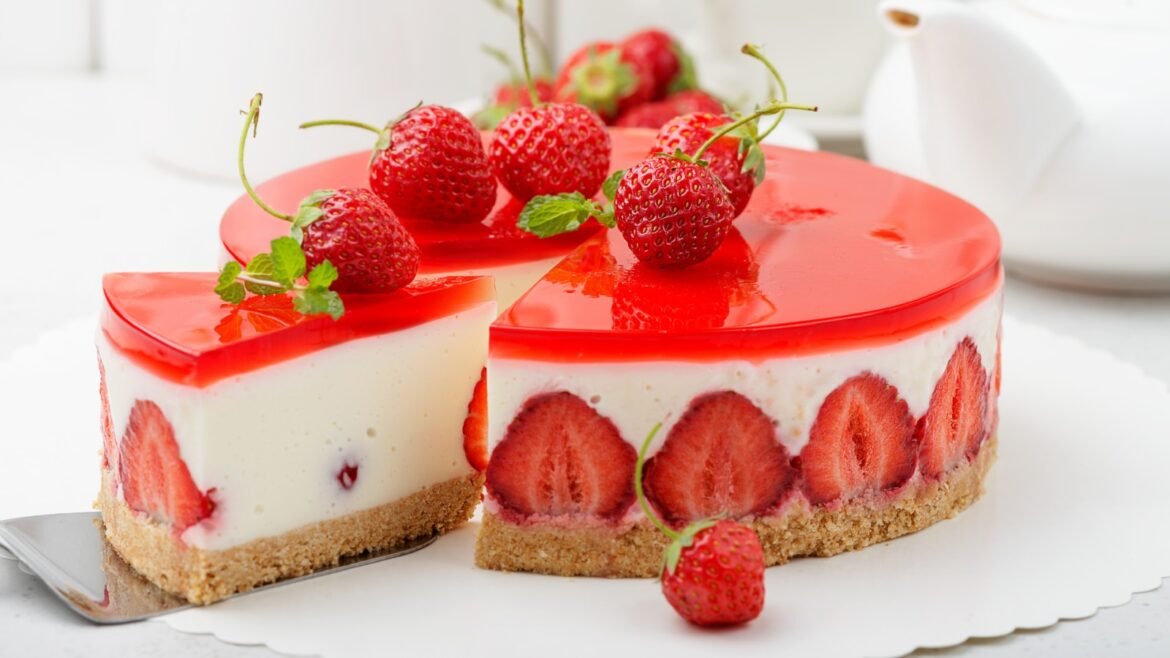 Strawberry cheesecake with a glossy red glaze, sliced to show strawberry layers and a crumb crust, topped with fresh berries and mint.