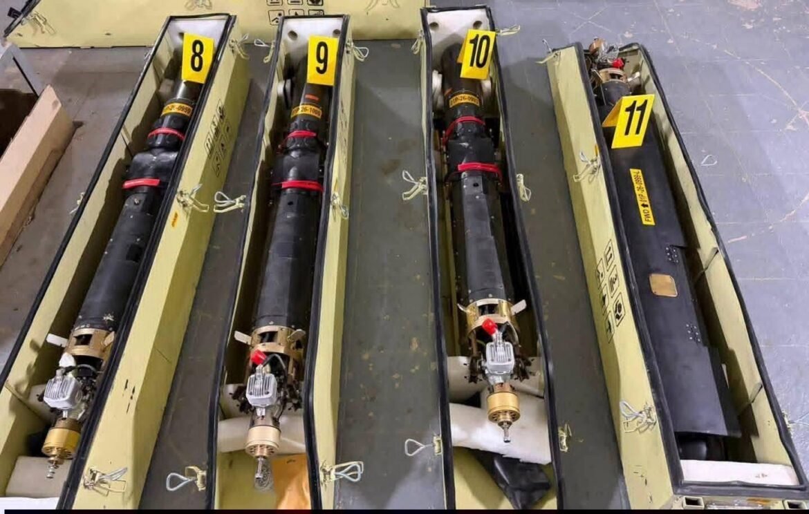Row of long black cylindrical equipment stored in yellow cases, labeled 8, 9, 10, and 11, with red restraints and metallic fittings at the ends.