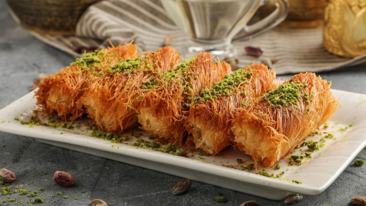 Sliced kataifi pastry dessert with shredded crust and crushed pistachios on a white plate