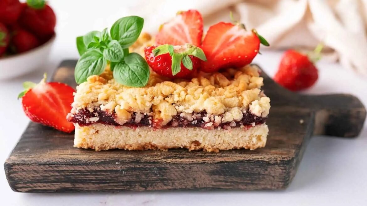 Strawberry crumble bar on a dark wooden board, garnished with fresh mint and halved strawberries on top.