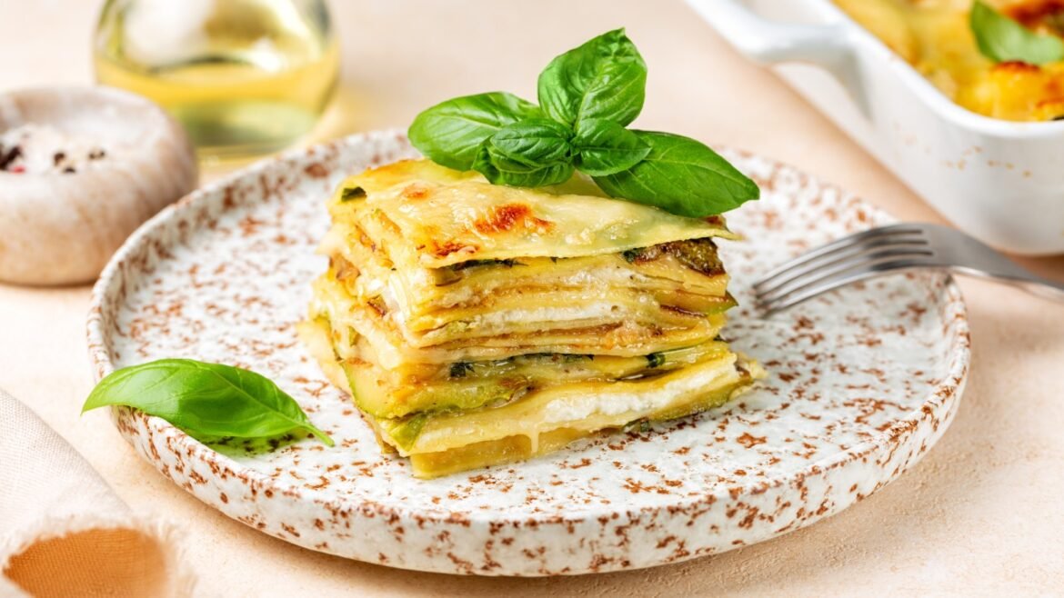 Stack of potato lasagna layered with cheese and herbs, garnished with fresh basil leaves on a speckled plate.