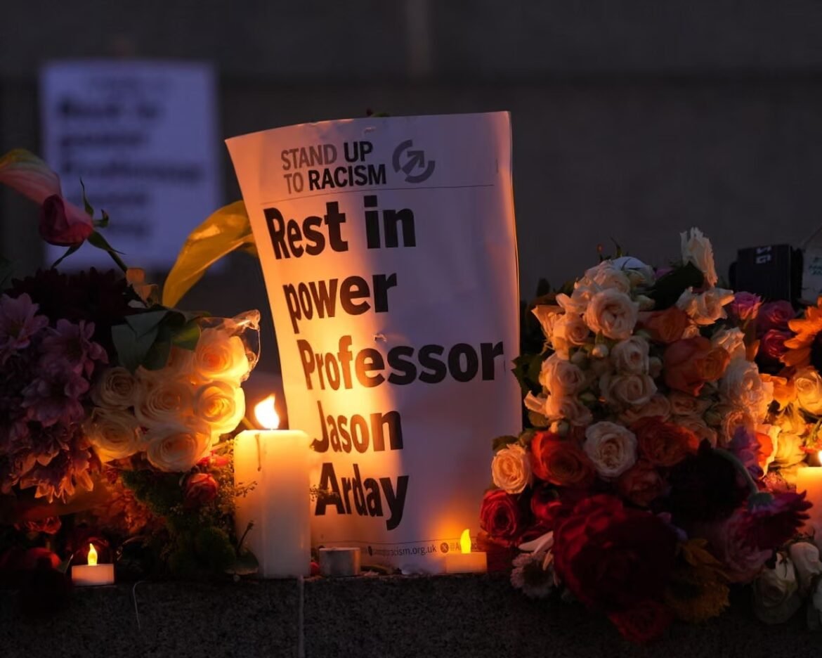 Candlelit memorial with bouquets surrounding a sign that reads 'Stand up to racism' and 'Rest in power Professor Jason Arday'