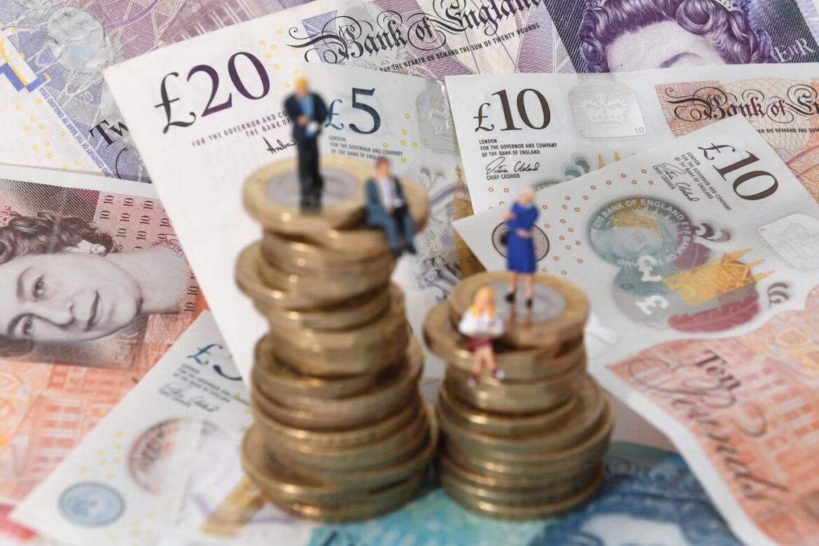 Miniature people stand on stacked coins with UK banknotes in the background, illustrating wealth and investment growth