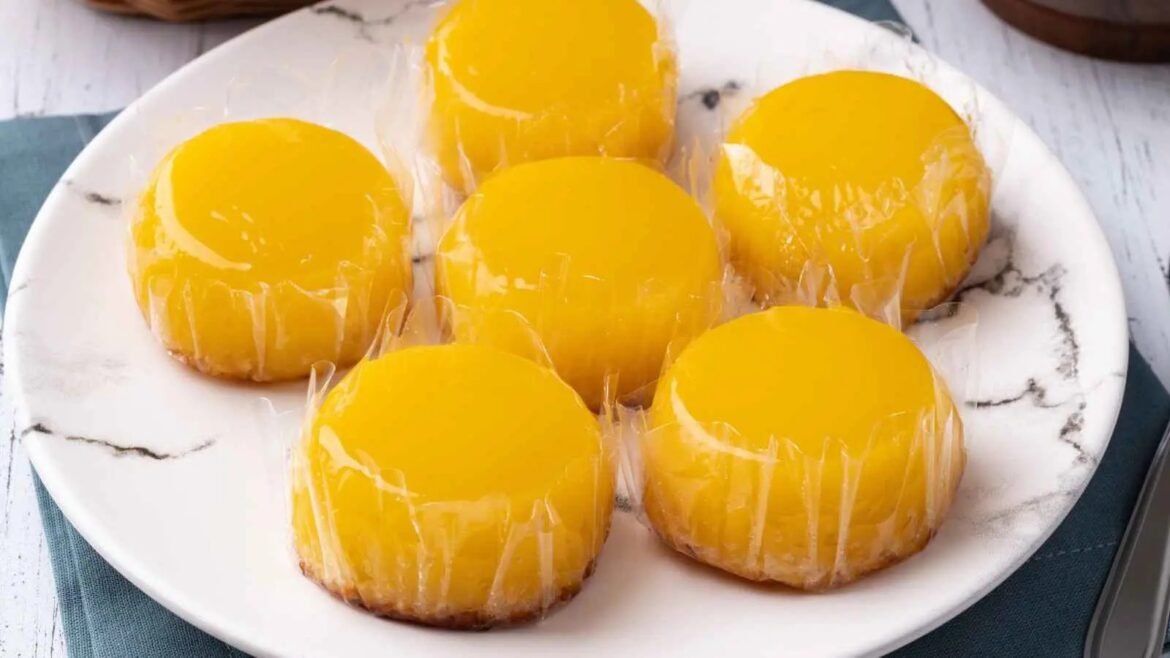 Seven individual mango desserts wrapped in plastic on a white marble plate.