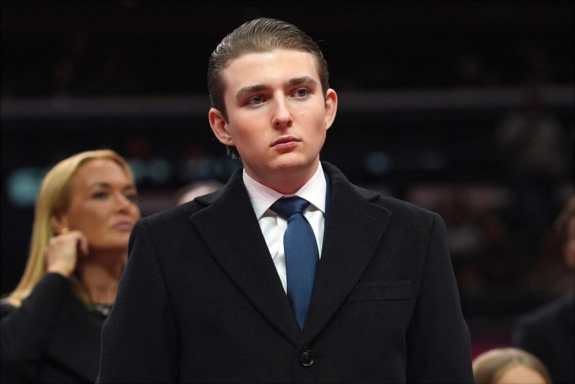 Young man in a dark overcoat and blue tie at an indoor event, looking to the side.