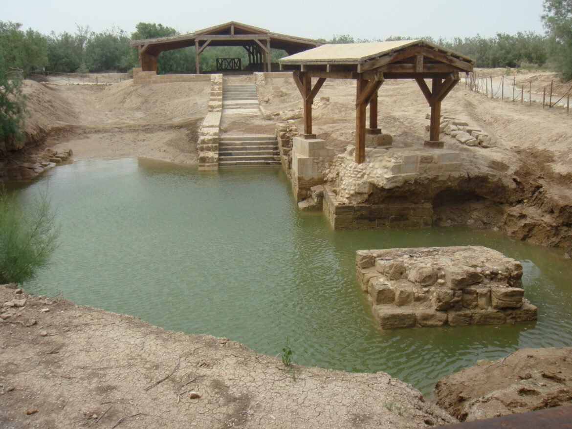 Wooden pavilion on stone platforms overlooking a calm, man-made pool with steps down to the water.