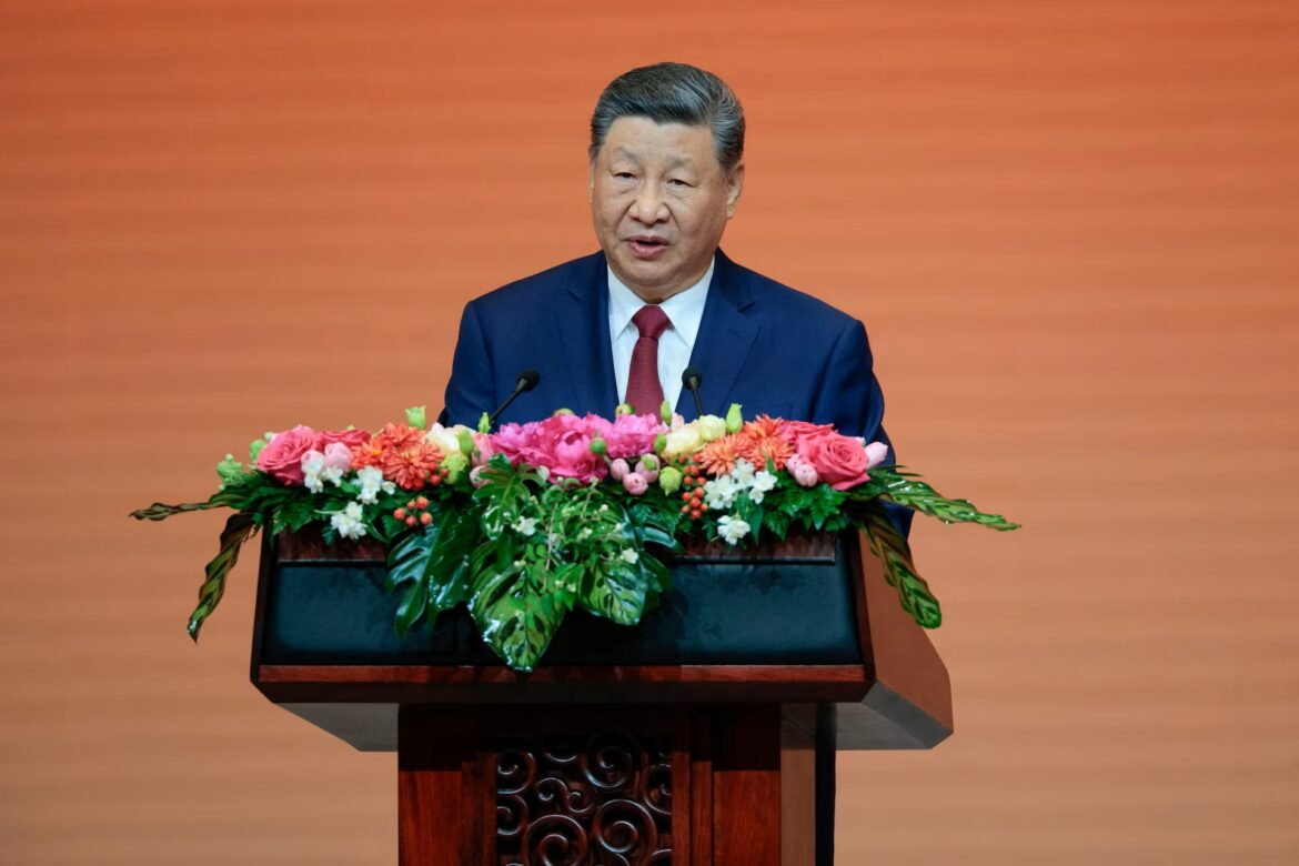 Man in a navy suit and red tie delivering a speech at a flower-adorned podium.