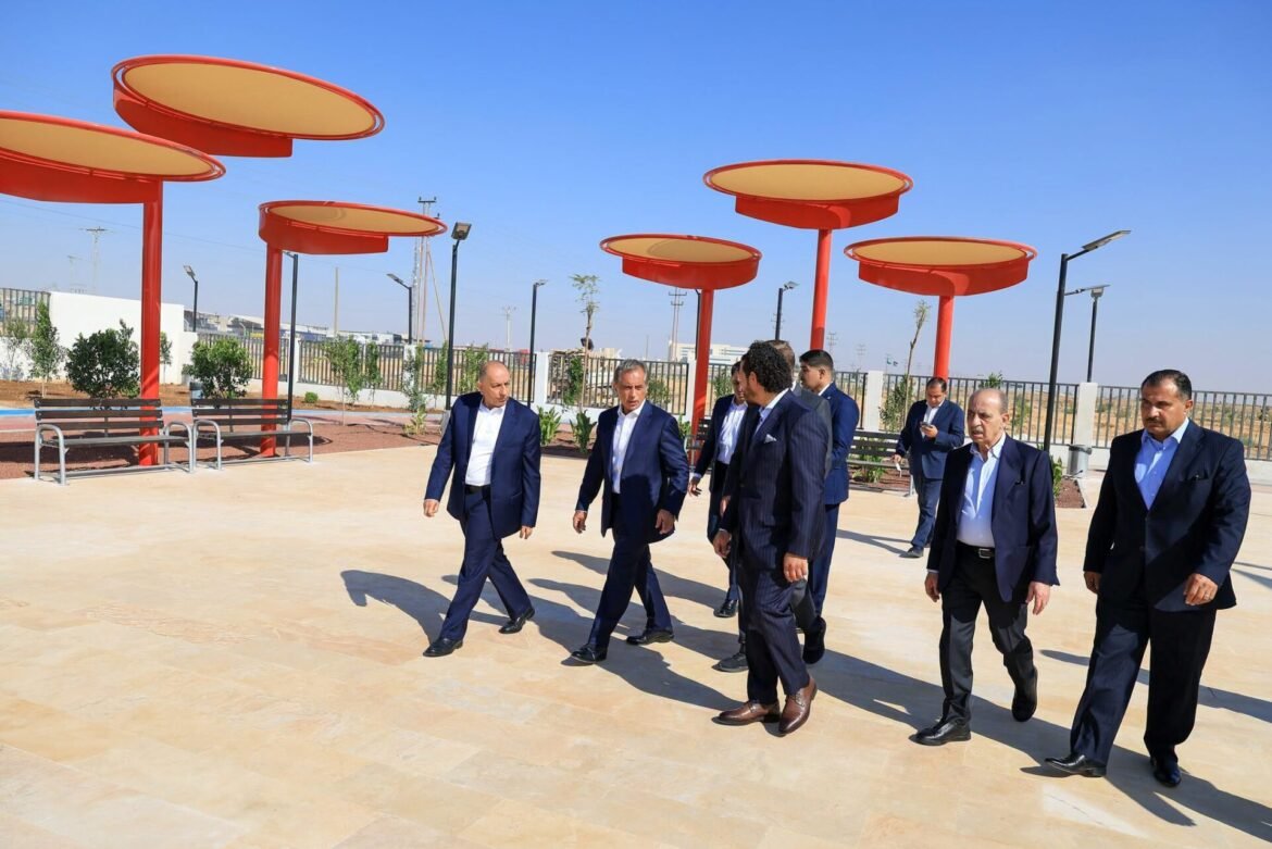 Group of men in dark suits walking across a sunny plaza with red circular shade canopies overhead under a clear blue sky.