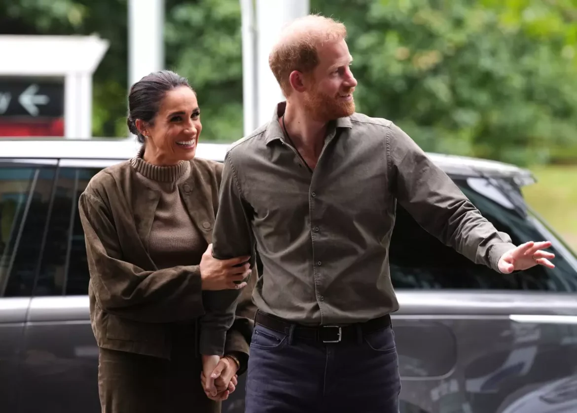 Smiling couple holding hands as they walk beside a dark SUV outdoors, the man extending an arm as if pointing or greeting.