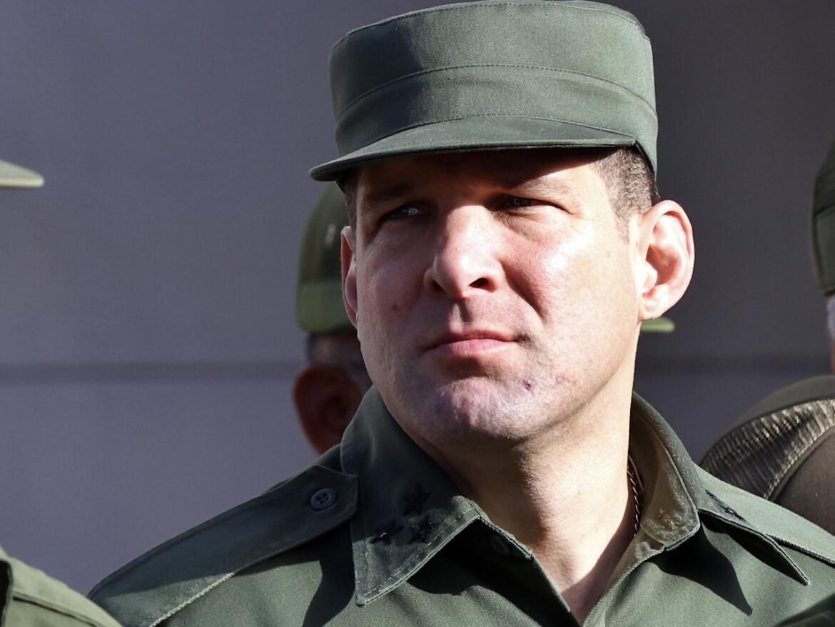 Close-up of a man in a green military uniform and cap, looking off to the right.