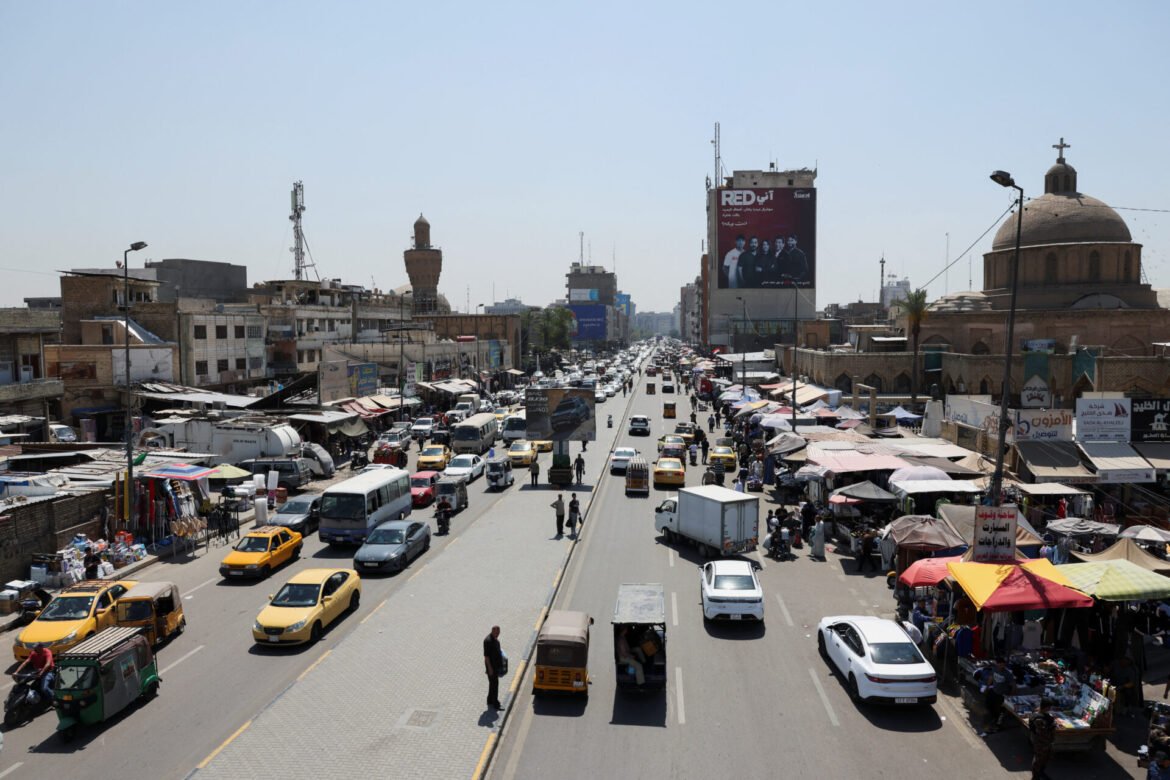 Busy city street lined with market stalls and dense traffic, pedestrians and cars in hurry under a clear blue sky.