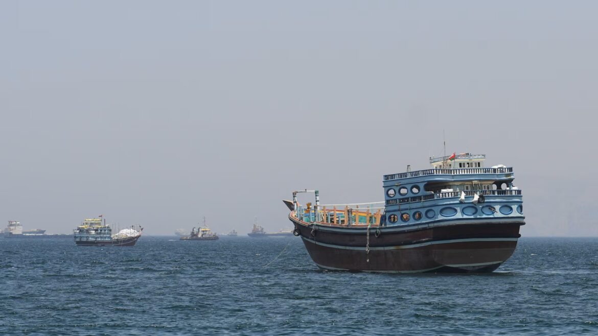 Large blue multi-deck passenger boat anchored in calm sea, with smaller boats in the distance against a clear sky.