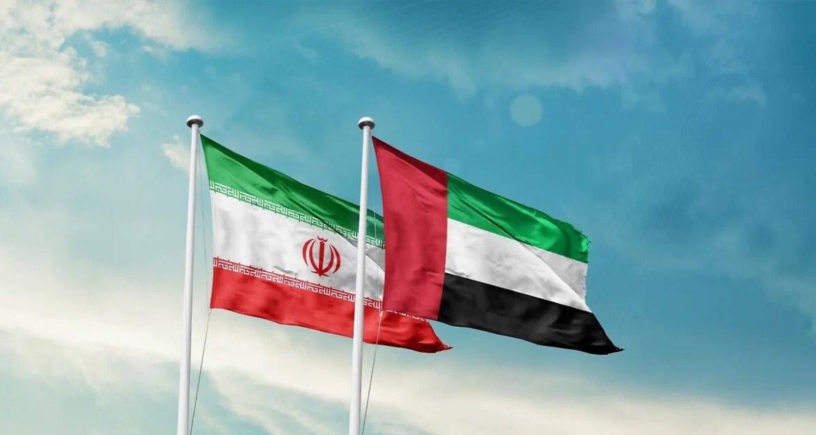 Two national flags—Iran on the left and the United Arab Emirates on the right—flown on flagpoles against a blue sky.