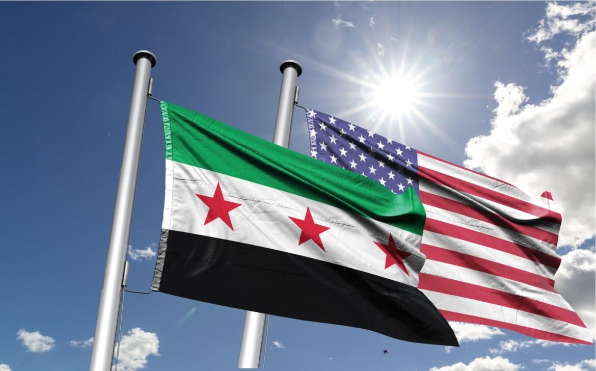 Two national flags (Syria and the United States) fly on flagpoles against a blue sky with sunlight.
