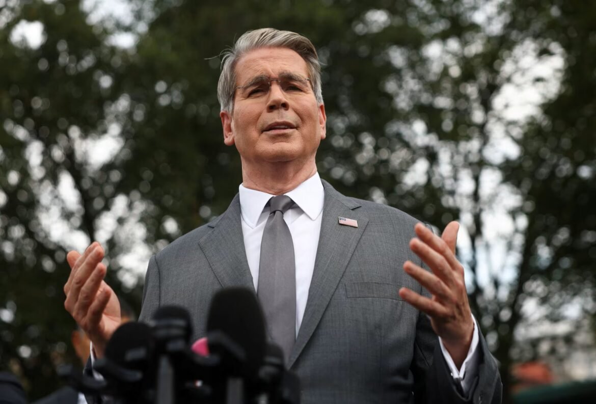 Man in a gray suit and tie speaks to reporters outdoors, hands raised as he addresses the press.
