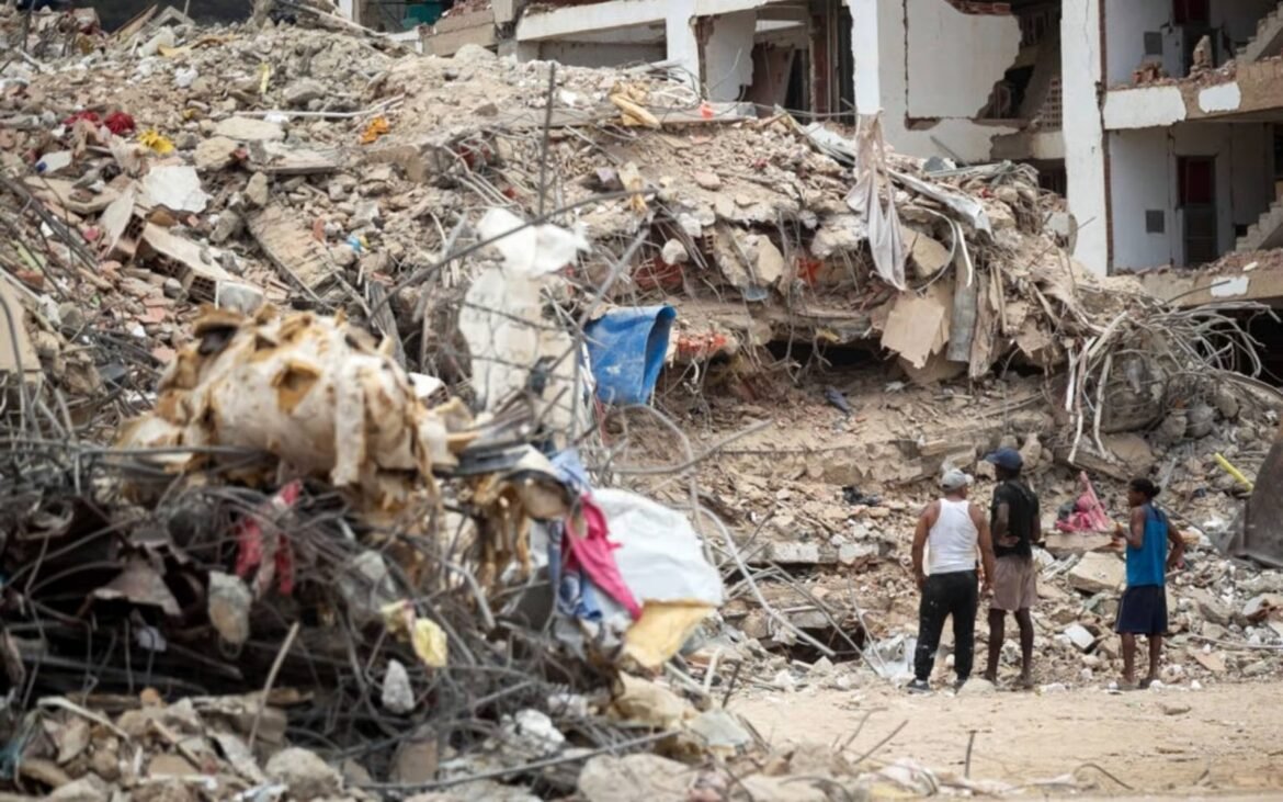 Four men stand amid rubble and destroyed buildings in an urban ruin, surveying the damage.