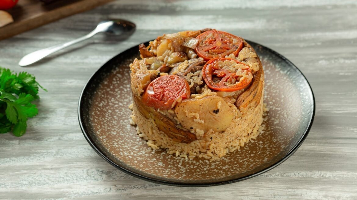 Round stack of seasoned rice with roasted potatoes, peppers, and tomato slices on a speckled brown plate.