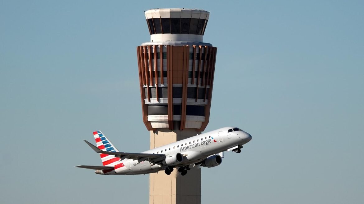 American Eagle jet taking off beside a tall air traffic control tower against a clear blue sky.