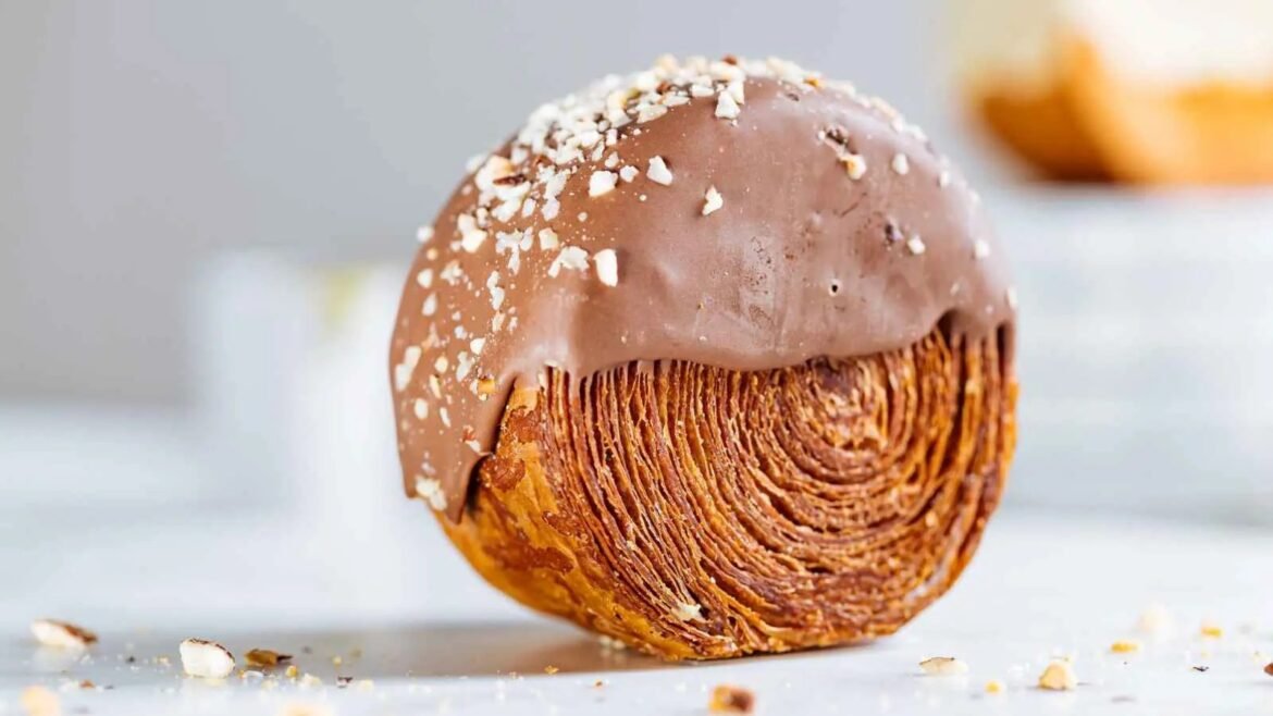 Close-up of a flaky chocolate croissant with glossy chocolate glaze and scattered almond pieces on top.