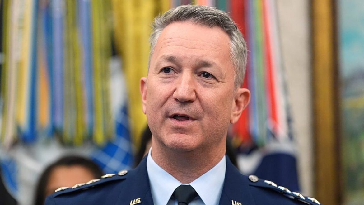 U.S. military officer in dress uniform speaking at an event, with colorful banners in the background behind him.
