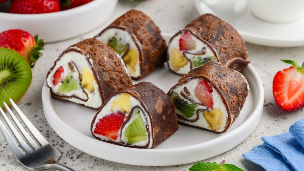 Chocolate Swiss roll slices filled with vanilla cream and mixed fruit (strawberry, kiwi, banana) on a white plate.