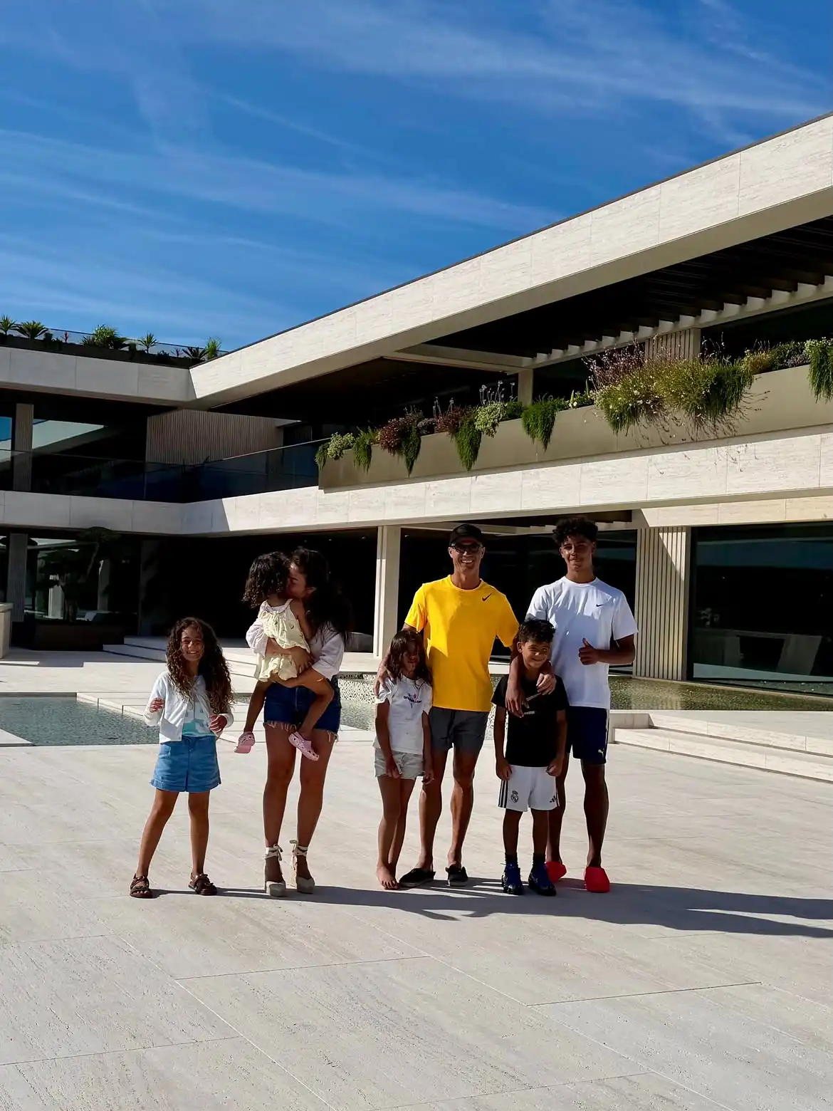 a Family of Seven Posing Together on a Sunny Terrace in Front of a Modern Building with Plants on the Balcony  Aleumumnews