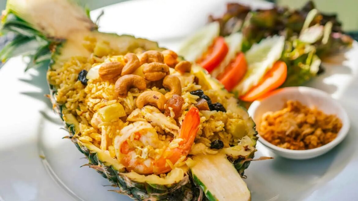 Pineapple half hollowed and filled with shrimp fried rice, cashews, and vegetables on a plate with a side salad.