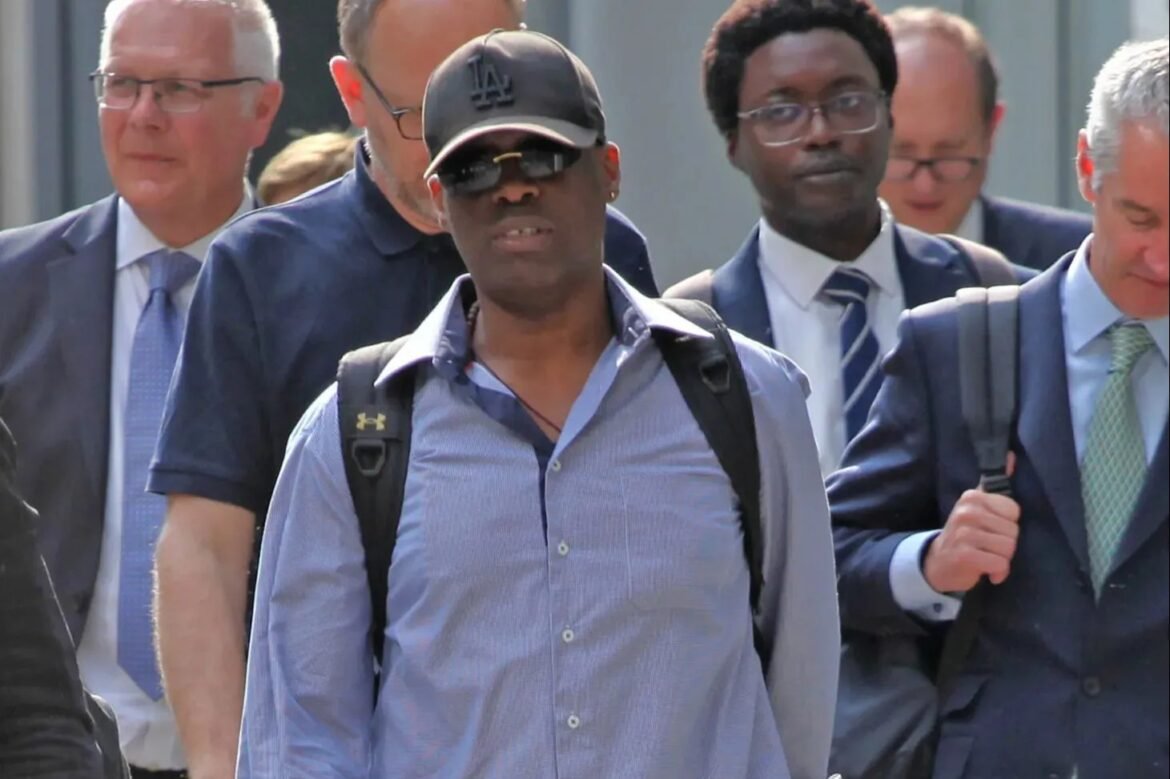 Man in a blue shirt, cap, and sunglasses leads a group of suited colleagues outdoors, with a backpack on his shoulders.