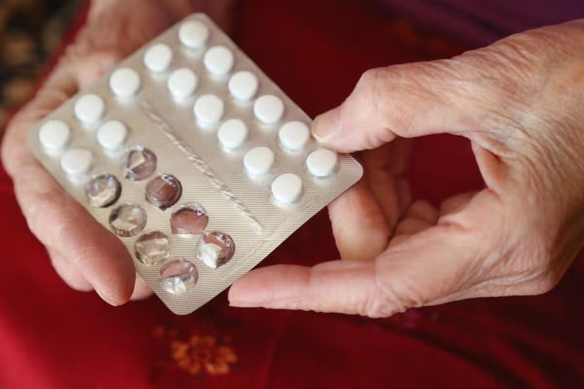 Elderly hands hold blister packs of white tablets, with several pills removed from one strip.