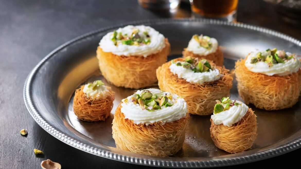 Kataifi pastry cups topped with whipped cream and chopped pistachios on a silver tray.