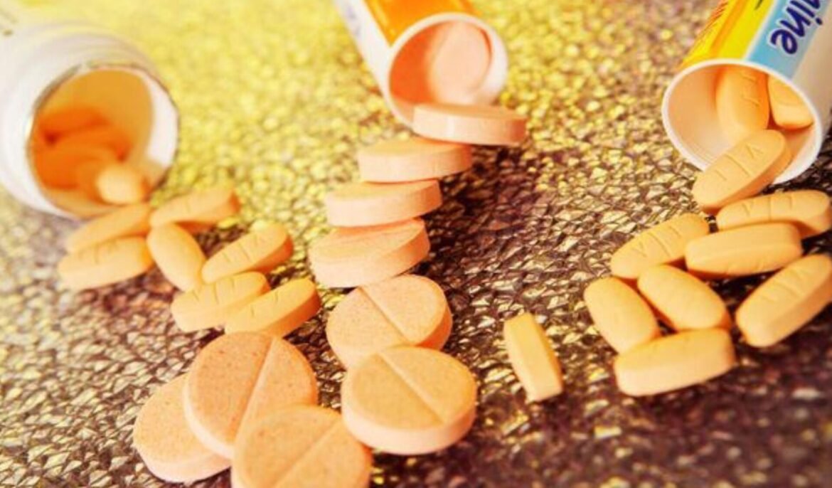 Orange tablets spilled from a white bottle onto a textured, speckled surface.