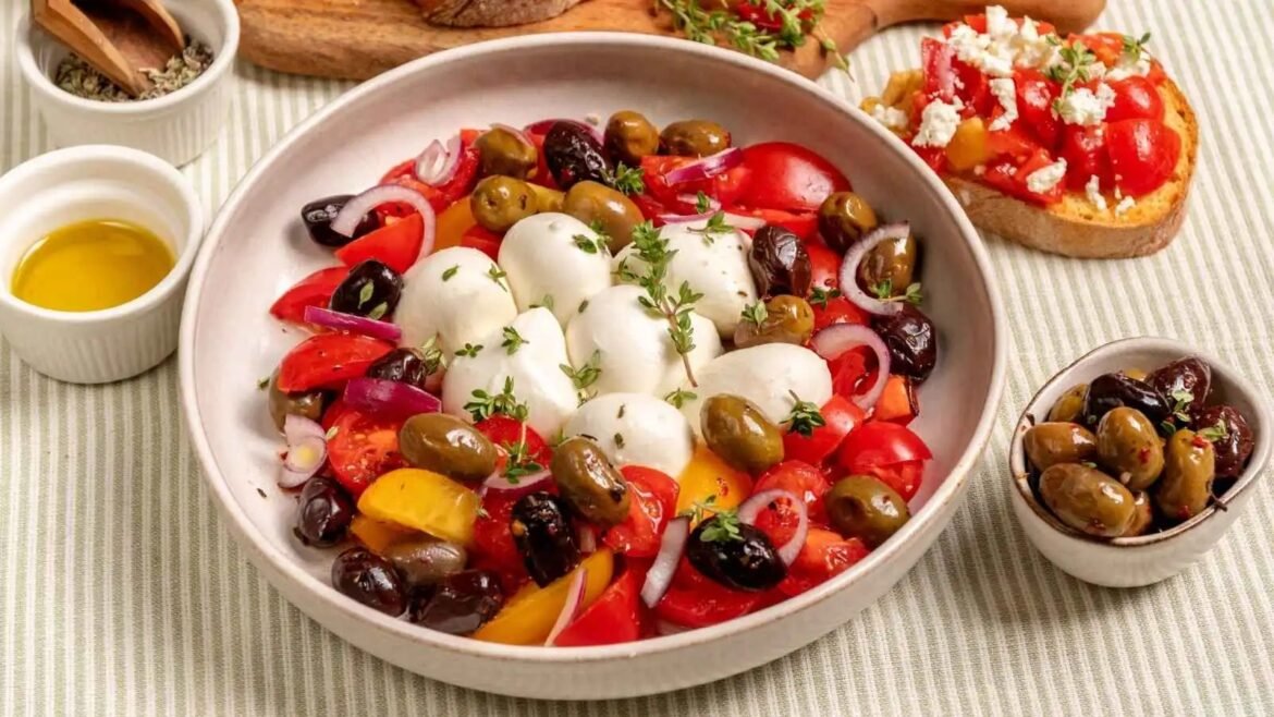 Bowl of Mediterranean salad with mozzarella balls, olives, cherry tomatoes, onions, and herbs.
