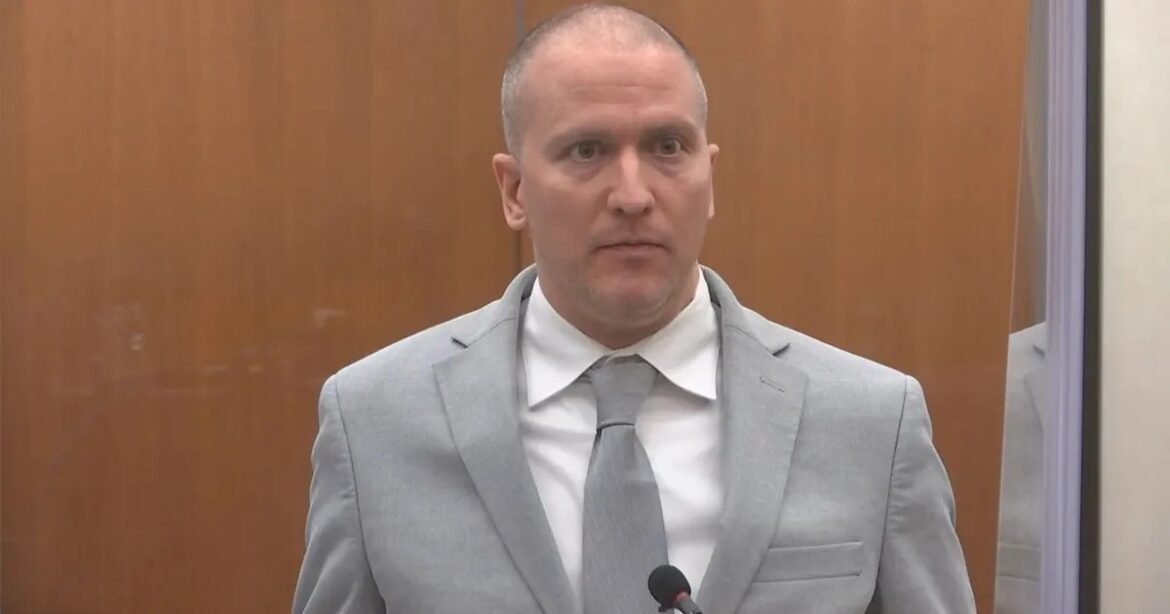 Man in a light gray suit and tie speaking into a microphone in a courtroom setting