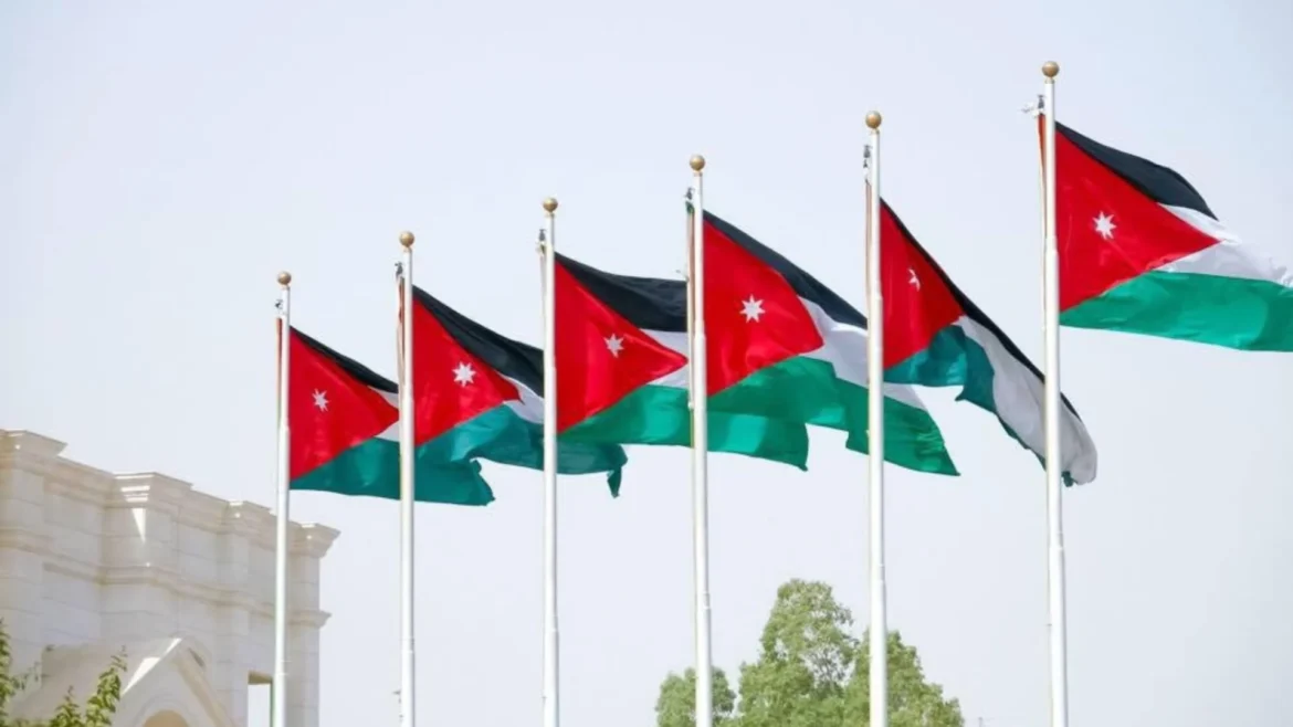 Multiple Jordanian flags flapping on flagpoles in front of a light-colored building.