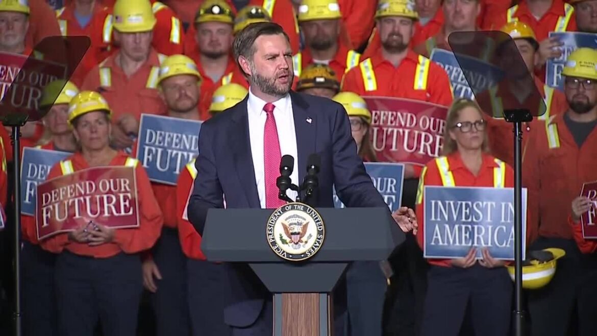 Speaker at a podium with the US seal, addressing a crowd of workers in orange safety vests holding 'Defend Our Future' and 'Invest in America' signs.