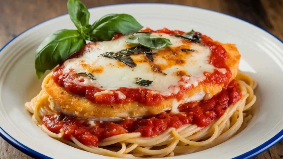 Plate of spaghetti topped with breaded chicken parmesan, tomato sauce, melted mozzarella, and basil leaves
