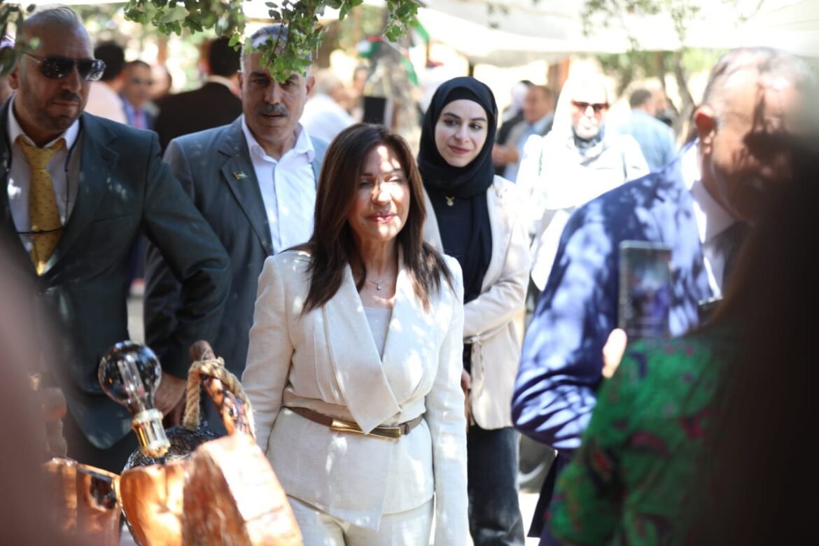 Group of people at an outdoor event, with a woman in a beige suit walking through the crowd.