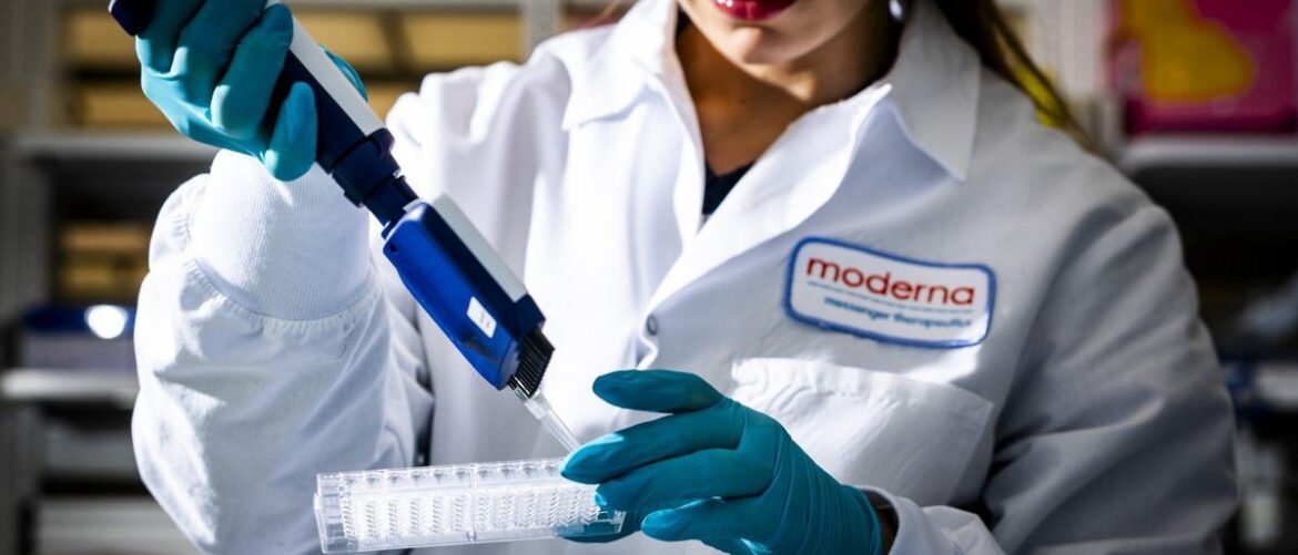 Scientist in a lab coat with teal gloves uses a pipette to transfer liquid into a clear tube rack labeled Moderna badge visible on the coat