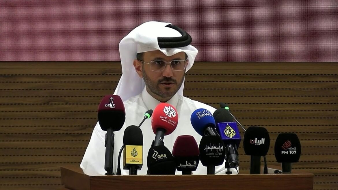 Man in a white thobe and ghutra speaks at a podium with many microphones in front of him at a press conference.