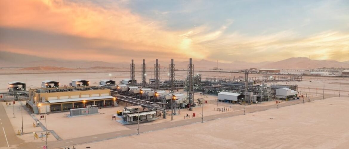 Oil refinery complex in a desert at sunset with tall distillation towers and pipelines nearby.