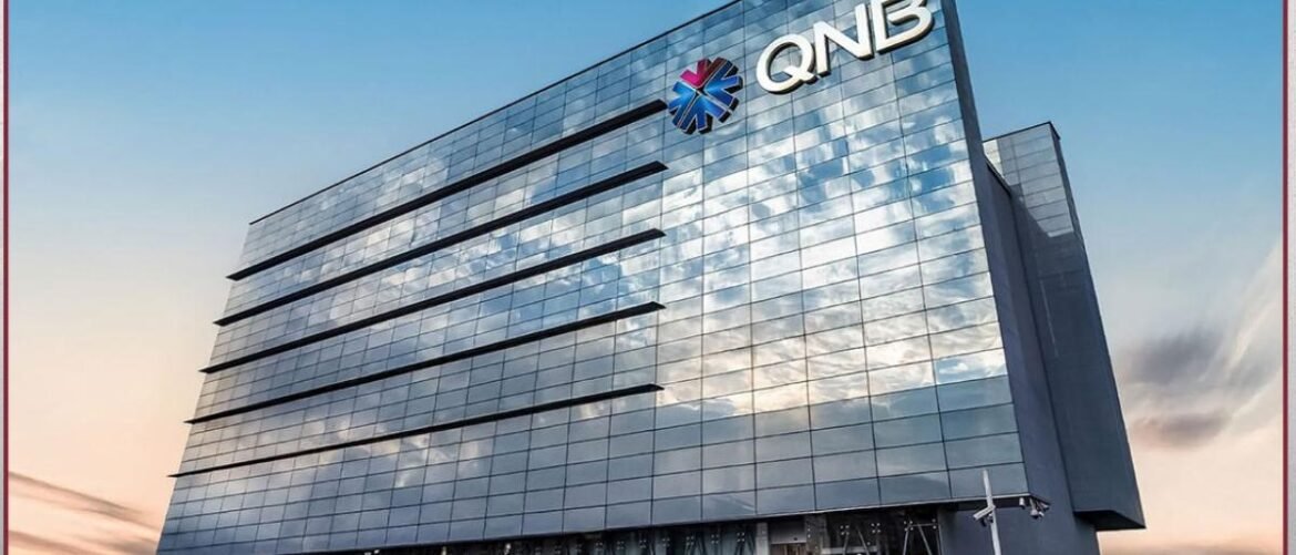 Modern glass office building with the QNB logo on the top corner against a blue sky view