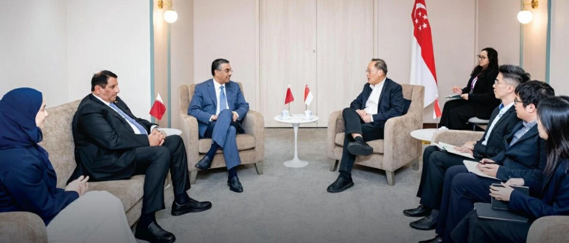 Formal diplomatic meeting in a neutral room, two groups of professionals seated on beige chairs around small tables with Singapore flags between them and a Singapore flag in the background.