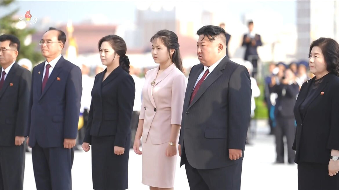 Group of formally dressed officials standing in a line during an outdoor ceremony, facing forward.