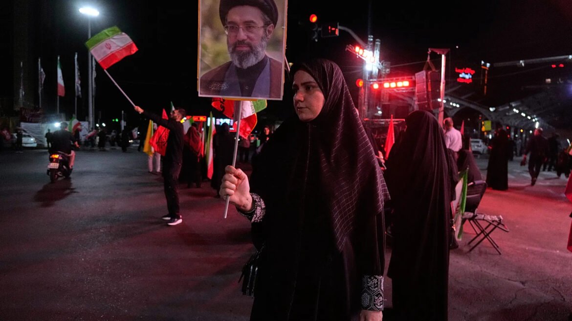 Woman in a black chador holding a portrait banner at a nighttime street protest.