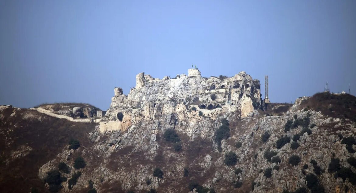 Ancient stone fortress ruins sit atop a rocky hill under a clear blue sky.