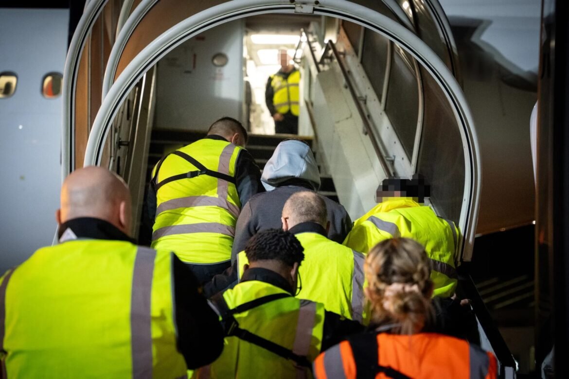 Group of passengers in high-visibility jackets boarding a plane through an aircraft door and stairs outside the cabin.